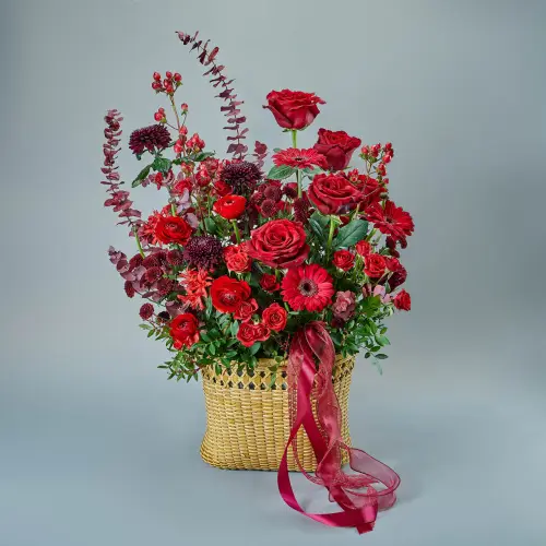 Композиция из микса красных цветов в плетеной корзине